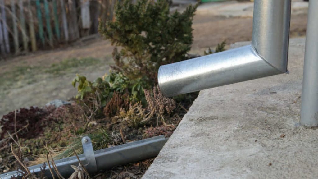 Vue rapprochée d'une gouttière métallique évacuant l'eau vers un canal de drainage au sol.