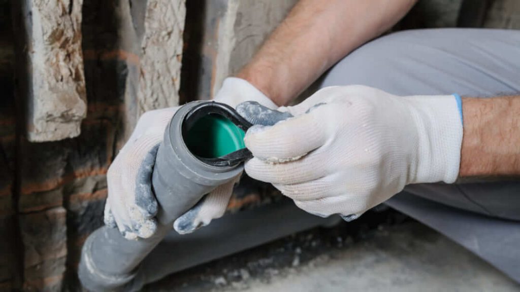 Gros plan sur des mains gantées installant un joint d'étanchéité dans un tuyau en plastique