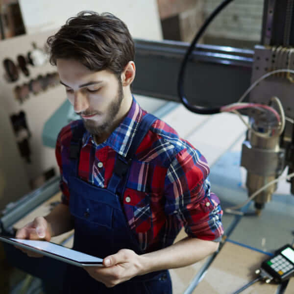 Un technicien en salopette utilisant une tablette numérique à côté d'une machine CNC industrielle.